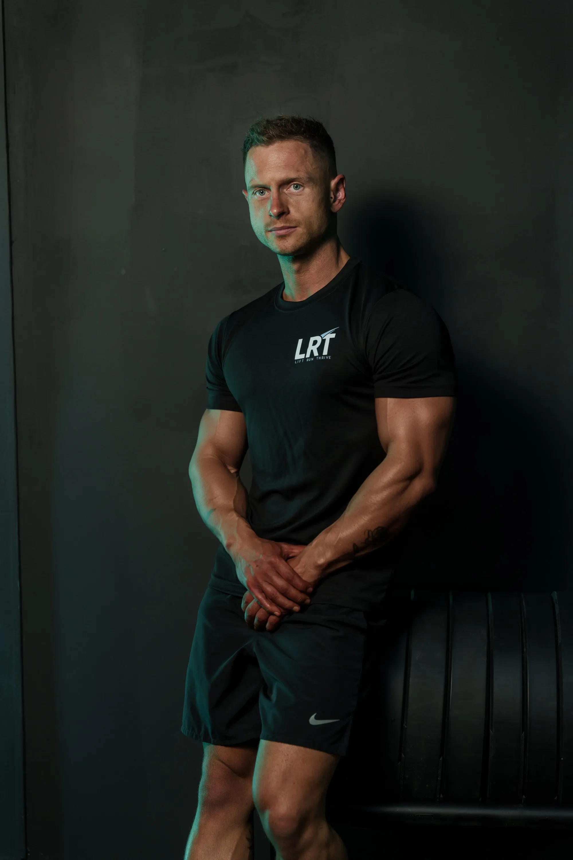 Callum Gilbert in a Lift Run Thrive t-shirt, leaning back against a dark wall